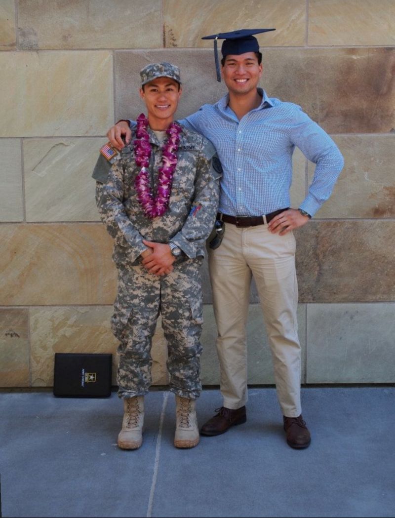 Ray in army fatigues with a flower lei around his neck, standing beside David in a graduation cap and gown.