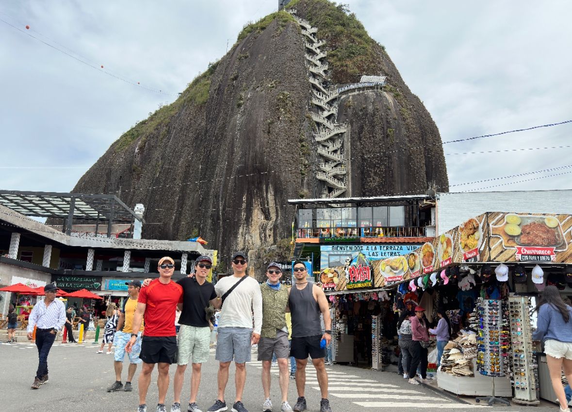Five friends standing together in front of the rock at Guatape, Colombia, its long stairway climbing behind them.